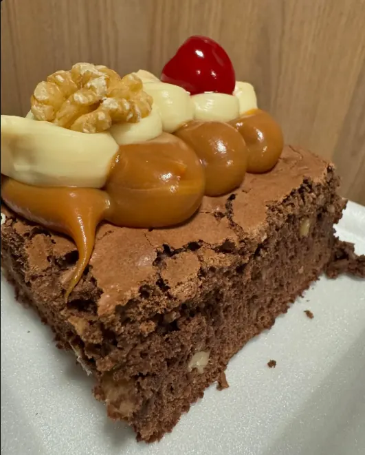 Porción de brownie con dulce de leche, crema, nuez y cereza